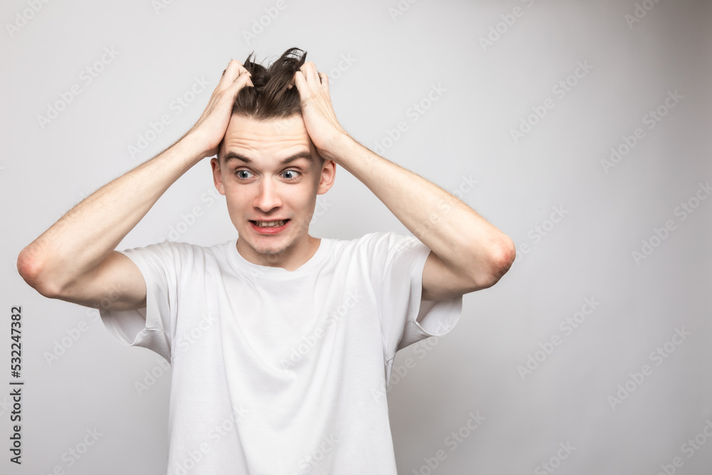 Confused young man holding his head studio shot on gray background Confused young man holding his head studio shot on gray background