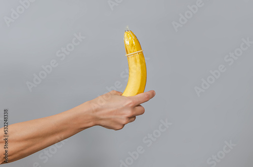 Slim female hand with banana and condom. Protected sex symbol.