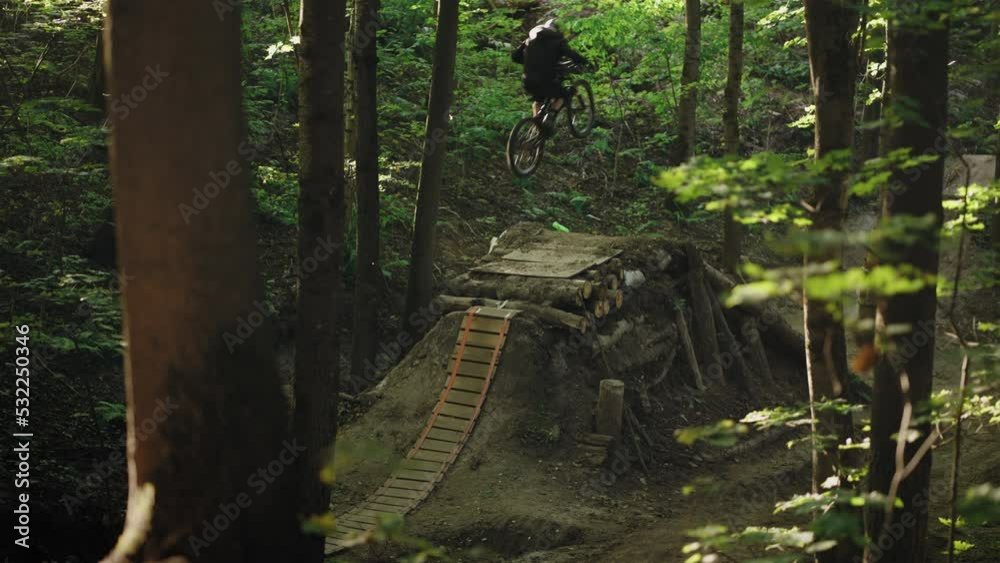 Cinematic Shot Long Focus Real Mountain Biker Jumping Over High Forest Springboard in Helmet Cinematic Shot Long Focus Real Mountain Biker Jumping Over High Forest Springboard in Helmet