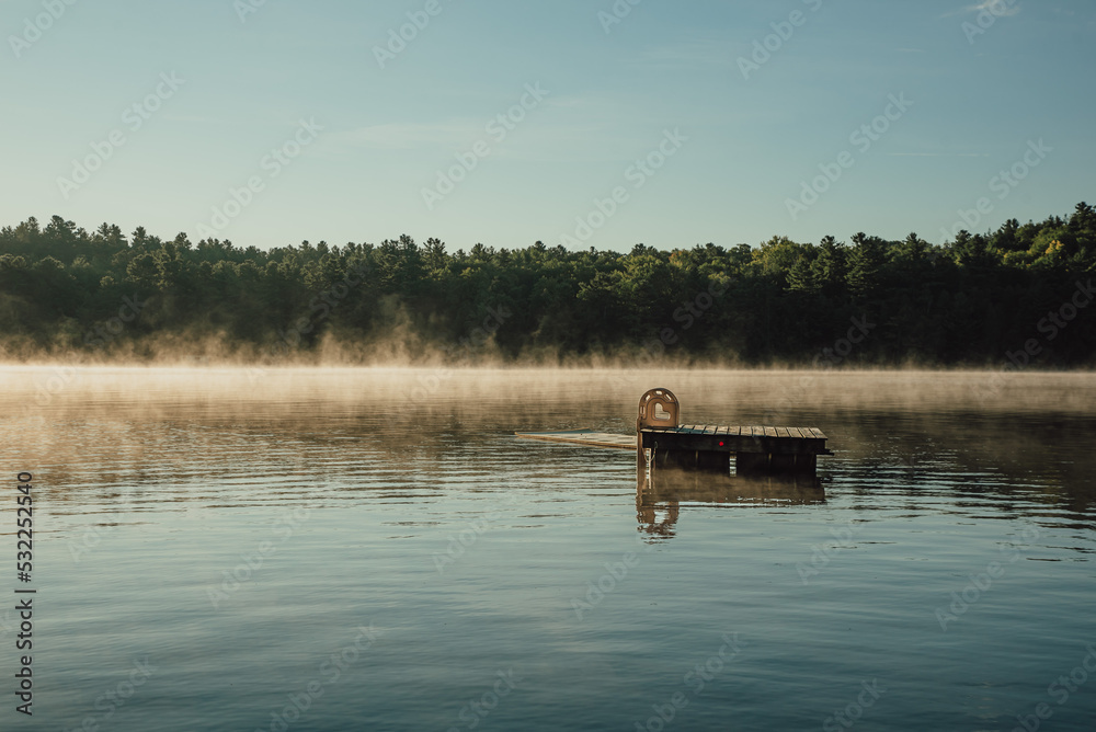 Swim platform floating on a quiet foggy lake at sunrise in Ontario, Canada.