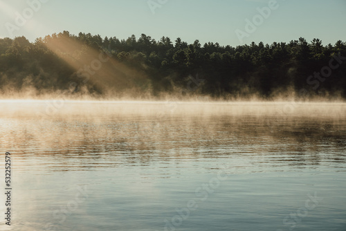 Fototapeta Naklejka Na Ścianę i Meble -  Morning sun shining on a quiet foggy lake in summer in Ontario, Canada.