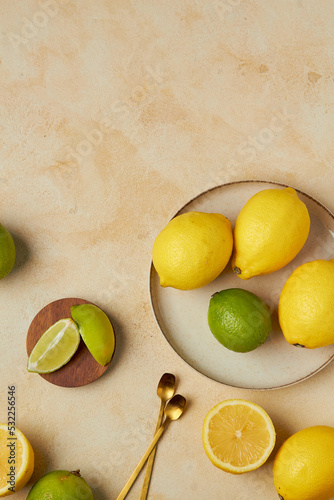 Plate with fresh citrus on beige background. Slice of lemons and limes with bottle of water and two spoons, top view, copy space photo