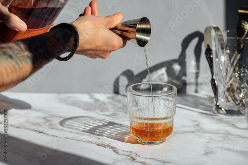 Picture of a person hand pouring whiskey ounce with a jigger on a cocktail glass