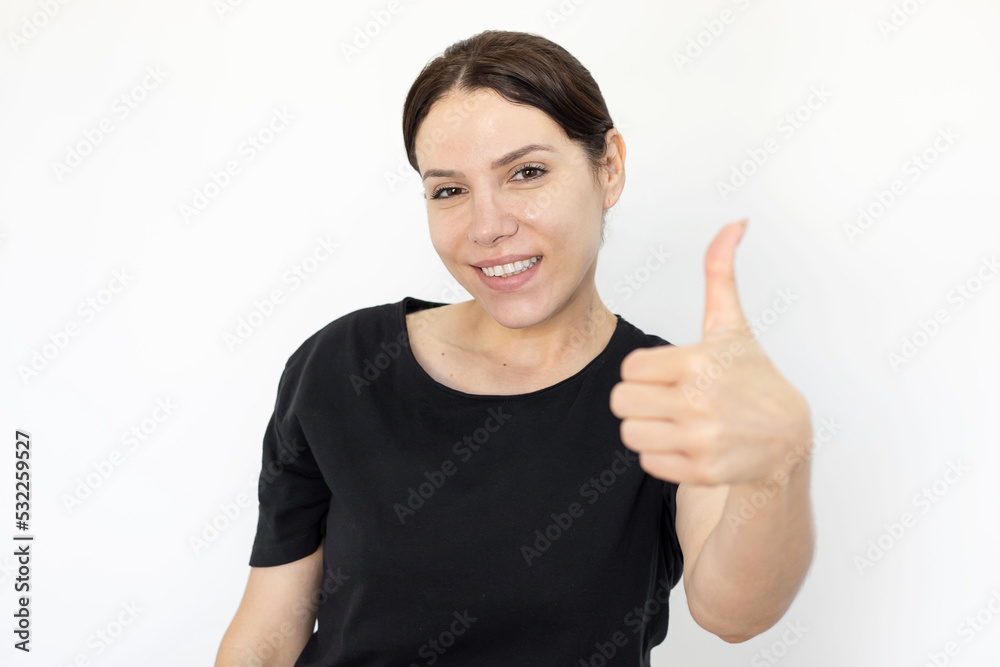 Cheerful woman showing thumbs up gesture. Portrait of Caucasian woman wearing black T-shirt, posing for camera and smiling against white background. Emotion, expression, gesture, studio shot concept Cheerful woman showing thumbs up gesture. Portrait of Caucasian woman wearing black T-shirt, posing for camera and smiling against white background. Emotion, expression, gesture, studio shot concept