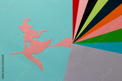 pink paper silhouette of the witch on the blue part of the background, from her broom comes out colorful art part of the background, halloween concept, flat lay, paper craft
