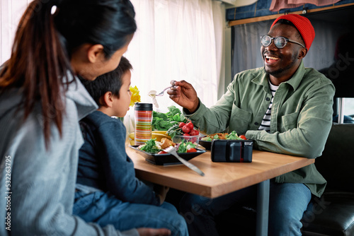 A multiracial family of three is eating a meal in a van.