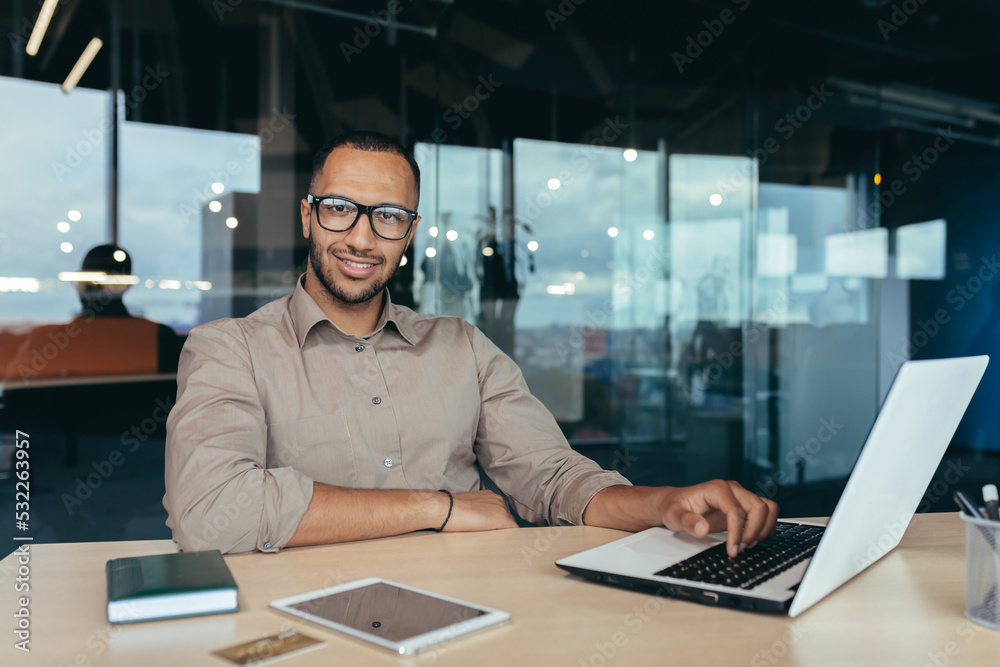 Portrait of successful businessman, man with laptop working inside modern office building, startup entrepreneur working with laptop, wearing glasses smiling and looking at camera. Portrait of successful businessman, man with laptop working inside modern office building, startup entrepreneur working with laptop, wearing glasses smiling and looking at camera.