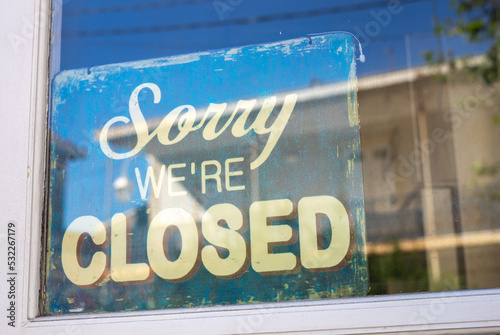 Sign in the shop window behind a pane of glass saying 'Sorry we're closed'. the shop is closed. end of business. closure of business. modern font. photo