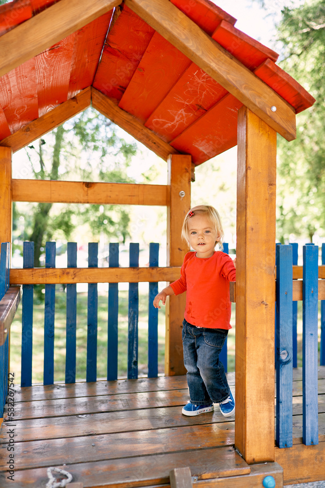 Obraz premium Little girl stands on a wooden platform under a canopy at the playground. High quality photo