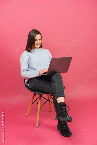 Young cheerful woman is sitting on a black chair and working on her laptop.