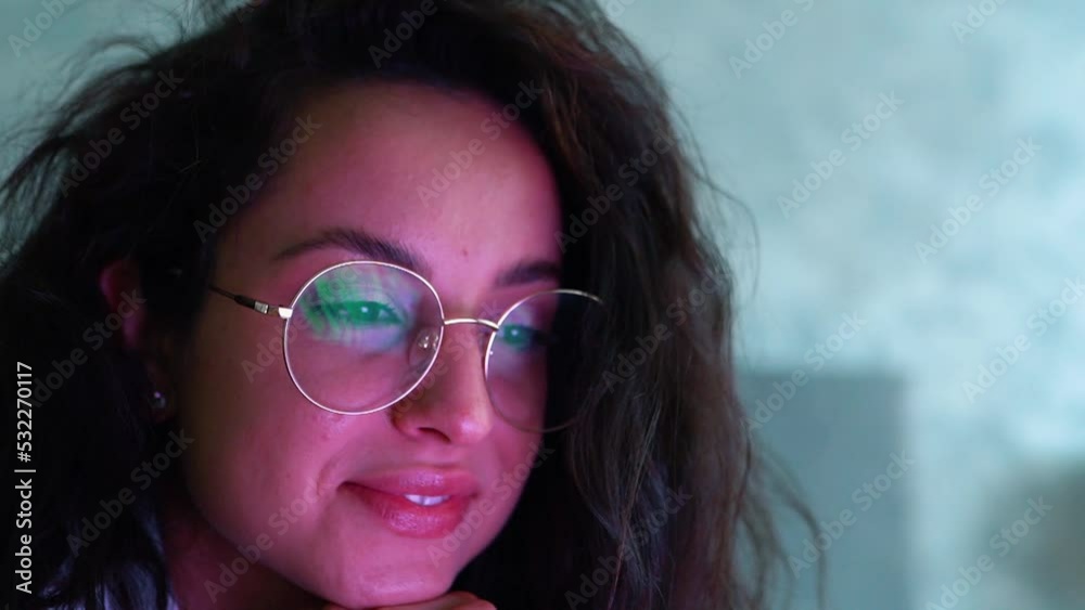 Young cheerful woman smiling while watching video on device online indoor. Close up shot. Slow motion. Laptop screen reflects in glasses on attractive happy female face. Leisure time Young cheerful woman smiling while watching video on device online indoor. Close up shot. Slow motion. Laptop screen reflects in glasses on attractive happy female face. Leisure time