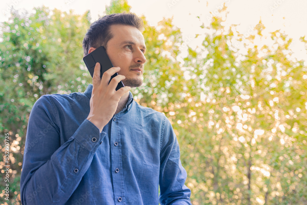 Portrait of young man talking on phone in city park. Young urban professional man using smart phone. Portrait of young man talking on phone in city park. Young urban professional man using smart phone.