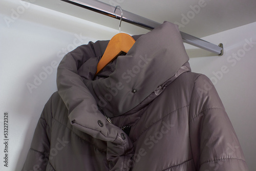 a down jacket on a hanger,a women's winter jacket hangs on a hanger in the compartment closet, a gray women's jacket is alone in the closet