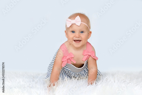 Adorable little baby girl in a dress and with a bow on her head creeping and playing in the home. White background.