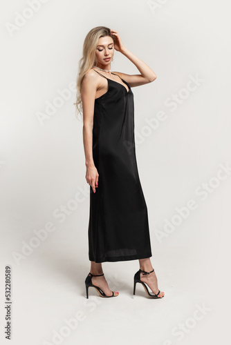 Beautiful fashionable elegant blonde woman with a slim sexy body in a fashion black dress with shoes heels posing in the studio on a white background