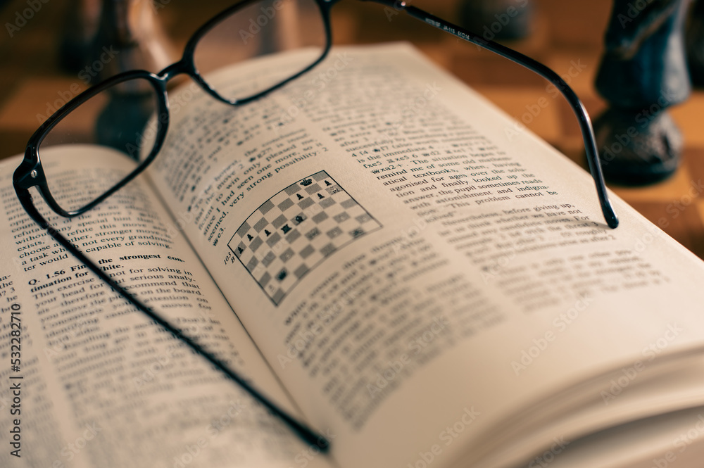 Self studying chess from a book, wooden chessboard and chess pieces Self studying chess from a book, wooden chessboard and chess pieces