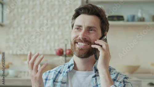 Bearded handsome man taking phone call from family while sitting on sofa at home. Fun communication with family and friends.