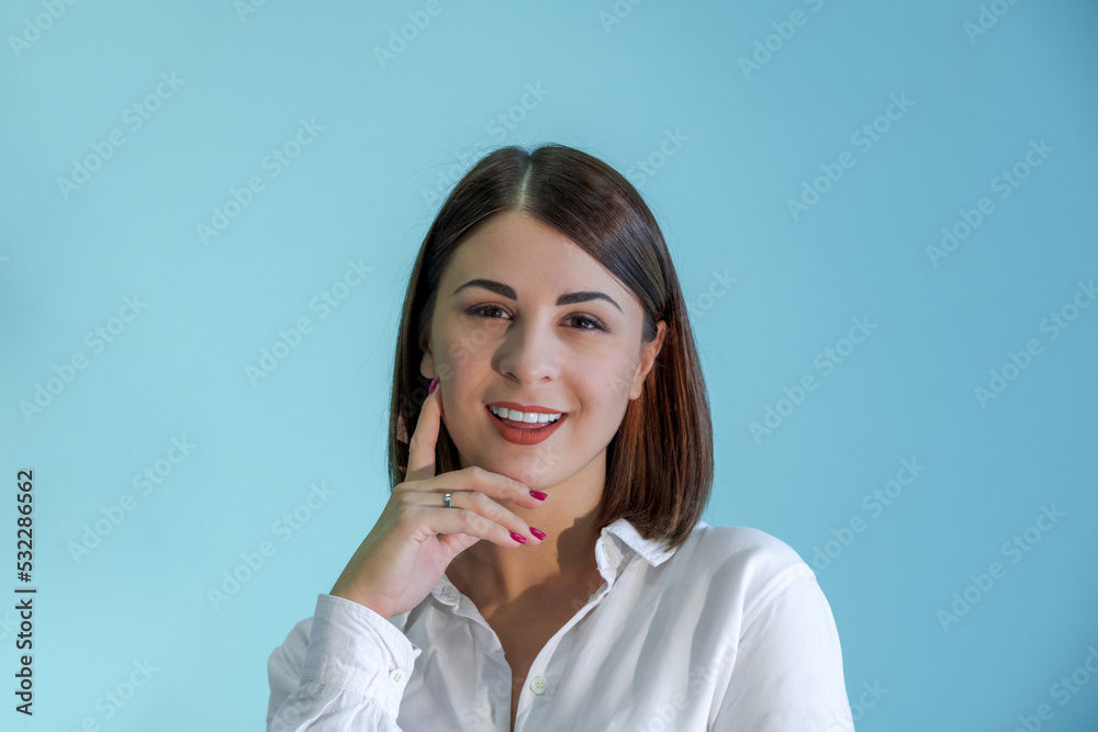 Close-up portrait of beautiful smiling caucasian woman with brown hair wearing white shirt. Blue background. Selective focus. People theme. Close-up portrait of beautiful smiling caucasian woman with brown hair wearing white shirt. Blue background. Selective focus. People theme.