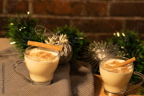 two eggnog cups, green garland with two silver balls, table in two heights with a light grey clown and red brick background with space for text. photo