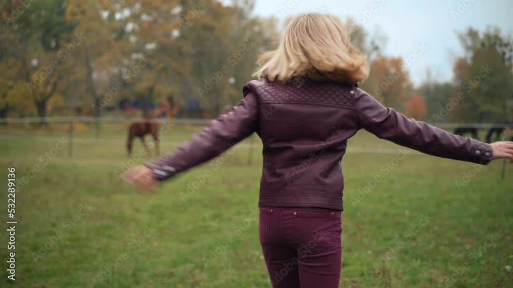 Joyful teenage girl spinning smiling on autumn meadow with horse barn at background. Portrait of excited carefree Caucasian teenager having fun outdoors enjoying weekend leisure Joyful teenage girl spinning smiling on autumn meadow with horse barn at background. Portrait of excited carefree Caucasian teenager having fun outdoors enjoying weekend leisure