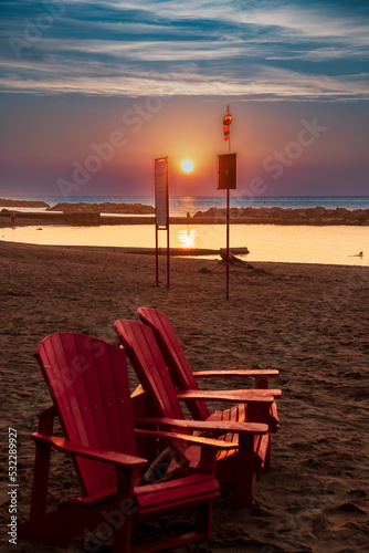 Photography Red Adirondak chairs on Kew Beach in Toronto with the sun rising in the background