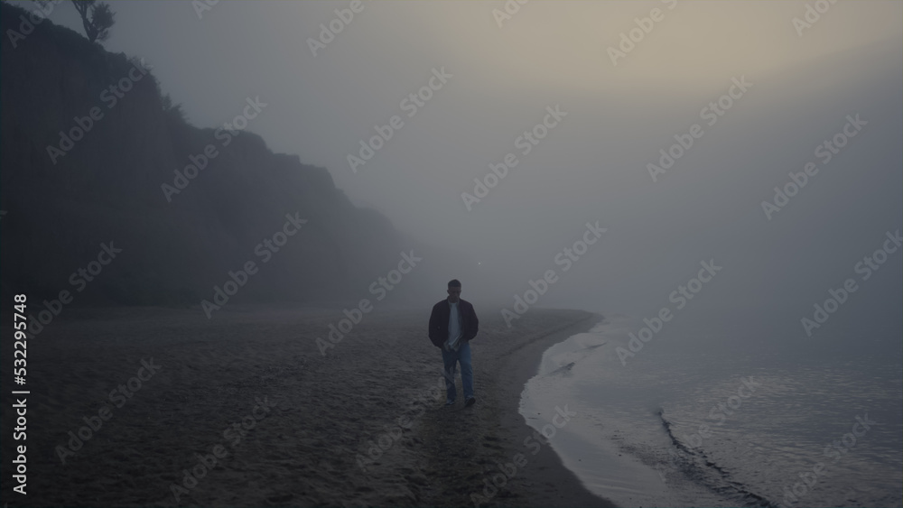 Lonely guy walking beach in foggy sunrise morning. Man exploring nature in mist