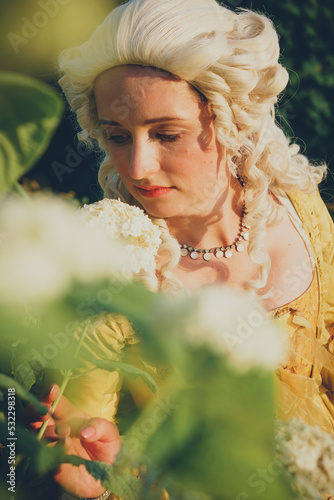 Portrait of blonde woman dressed in historical Baroque clothes with old fashion hairstyle, outdoors. Golden color dress. Luxurious medieval dress