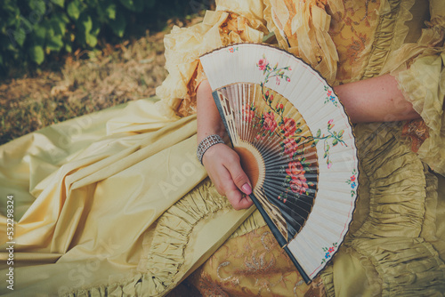 Luxurious medieval hand fan in the female hand, close up. Baroque accessory. Selective focus