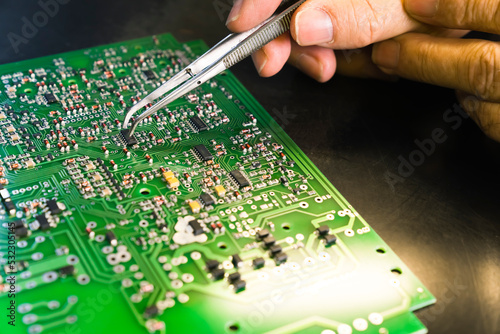 Repairing process of a broken PCB. Professional caucasian engineer manually removing broken electric components and replacing them with new ones with tweezer. Closeup shot. High quality photo