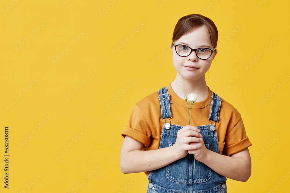 Waist up portrait of teen girl with Down syndrome looking at camera against yellow background in studio Waist up portrait of teen girl with Down syndrome looking at camera against yellow background in studio