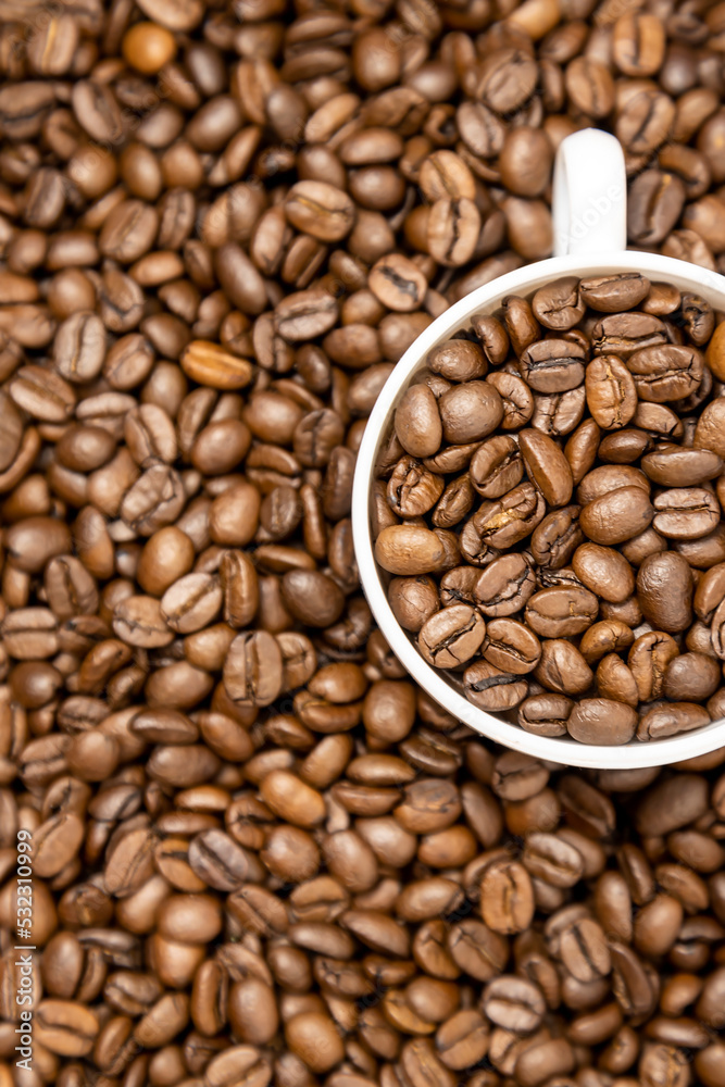 Vertical photo of a cup of coffee full of coffee beans. Top view of white cup and roasted coffee beans. Vertical photo of a cup of coffee full of coffee beans. Top view of white cup and roasted coffee beans.
