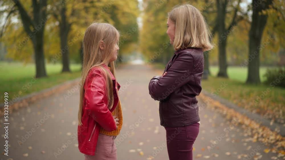 Side view positive girls talking standing on alley in overcast autumn park. Happy cheerful Caucasian friends meeting outdoors enjoying weekend day. Relaxation and friendship Side view positive girls talking standing on alley in overcast autumn park. Happy cheerful Caucasian friends meeting outdoors enjoying weekend day. Relaxation and friendship