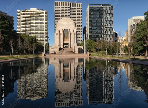 Northern side of Anzac Memorial in Hyde Park with pool of reflection reflecting the memorial and Sydney city high rise buildings. Deep blue sky.