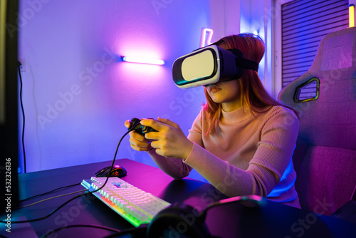 Excited woman virtual playing gamepad controller she very determined at home, Gamer in VR headset glasses exploring metaverse play video game online with joystick on computer neon lights