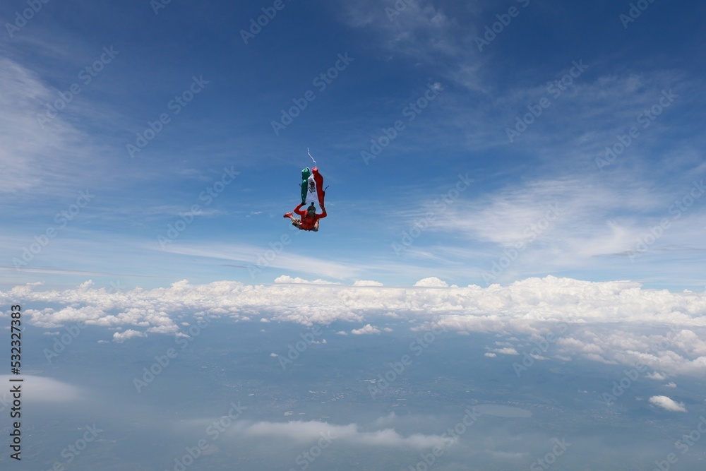 The national flag of Mexico is in the sky. A red skydiver is flying in the sky with Mexican flag.