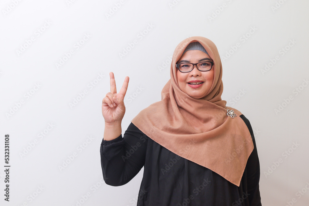 Portrait of cheerful Asian woman with hijab making fun face with peace ...