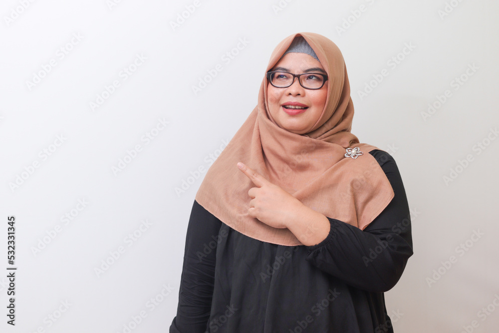 Portrait of cheerful Asian woman with hijab, showing product, pointing at something and smiling. Advertising concept. Isolated image on white background Portrait of cheerful Asian woman with hijab, showing product, pointing at something and smiling. Advertising concept. Isolated image on white background