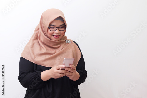 Portrait of cheerful Asian woman with hijab, holding mobile phone and feeling excited. Advertising concept. Isolated image on white background