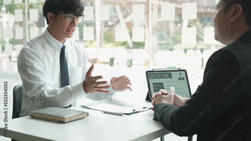 Asian young adult sitting at desk across from manager being interviewed job interview in business room. Asian young adult sitting at desk across from manager being interviewed job interview in business room.