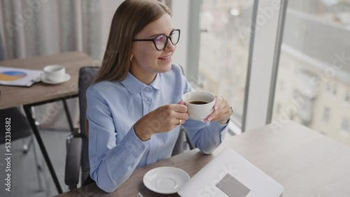 A little break from work to have a cup of coffee. Business lady drinks coffee sitting in the office enjoying view from panoramic window. photo