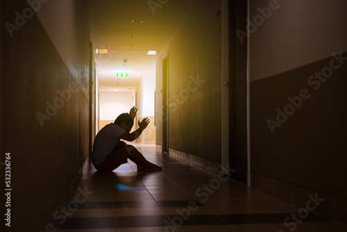 Fototapeta Naklejka Na Ścianę i Meble -  Depressed man sitting on the floor with his head down, silhouette of stressed young man holding his head in the hallway
