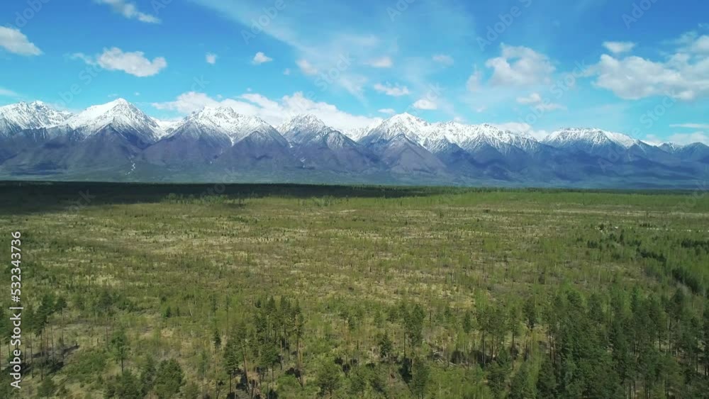 Aerial panoramic landscape of snow capped Sayan Mountains, valley and green forest on a bright sunny day. Picturesque scenery of Siberian nature Aerial panoramic landscape of snow capped Sayan Mountains, valley and green forest on a bright sunny day. Picturesque scenery of Siberian nature