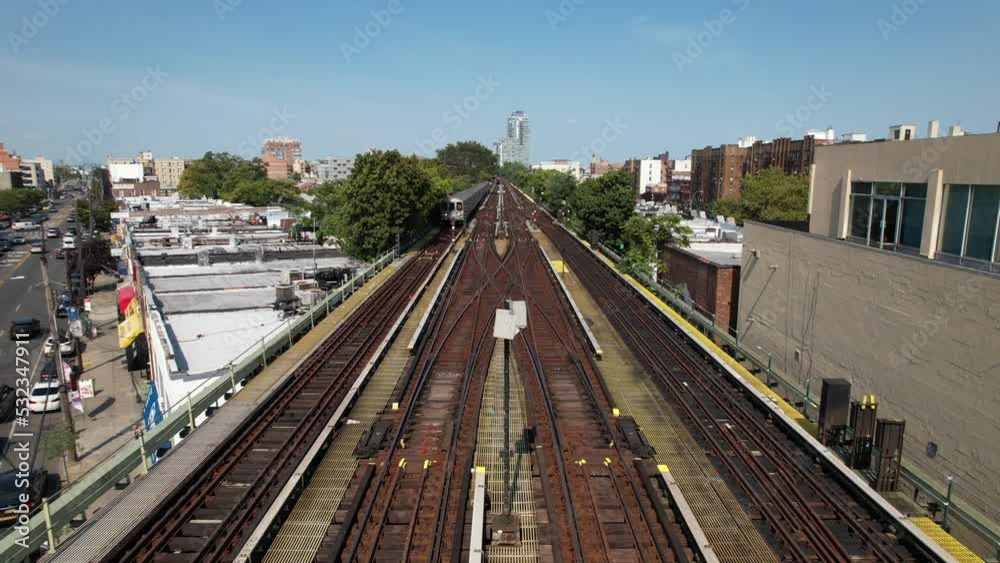 An aerial view of train tracks with a train travelling towards the camera on a sunny day. The camera is stationary over the center of the elevated tracks. An aerial view of train tracks with a train travelling towards the camera on a sunny day. The camera is stationary over the center of the elevated tracks.