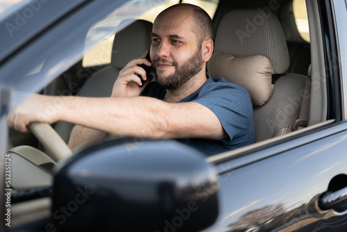 Portrait of smiling adult man driving car speaking on cellphone.