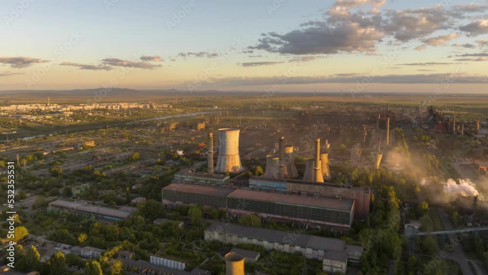 Circling aerial hyperlapse focusing a metal recycling factory emitting vapors at sunset.