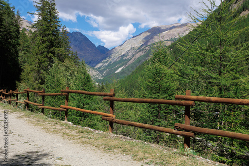 Path with Wooden Fence and in the background Mountain of the Italian Alps and Blue sky with Clouds
