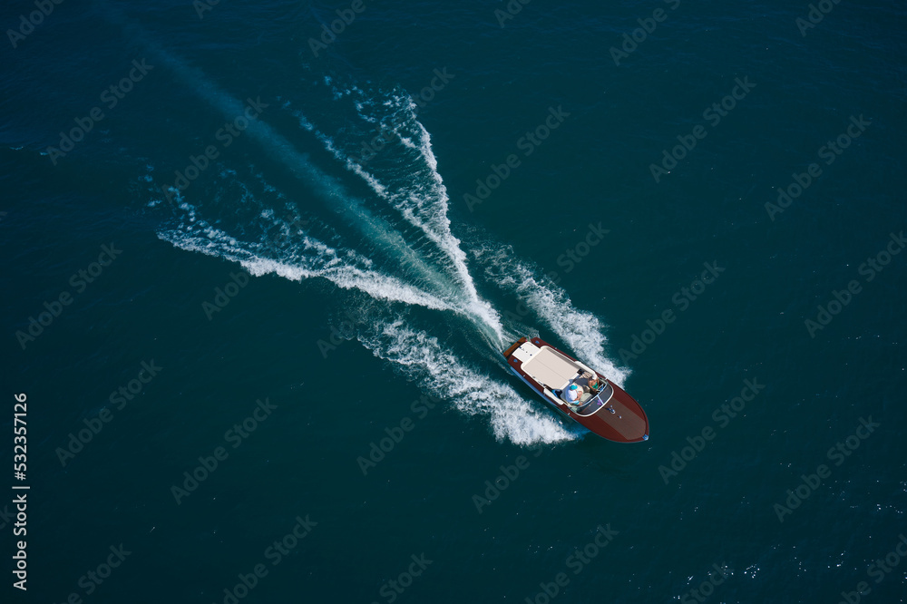 Obraz premium Luxurious wooden motor boat rushes through the waves of the blue Sea. Classic Italian wooden boat fast moving aerial view. Luxurious wooden boat fast movement on dark water.