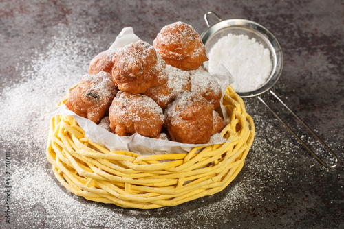 Sweet donuts oliebollen with raisins and powdered sugar close-up in a basket on the table. Horizontal photo