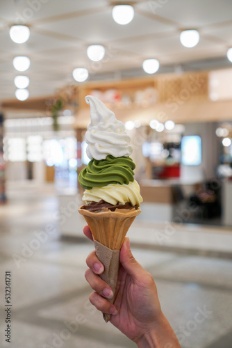 Soft serve ice cream tower. Woman hand holding a cone of four ice cream flavors with Hokkaido milk, matcha, yuzu sorbet and dark chocolate.(horizontal)