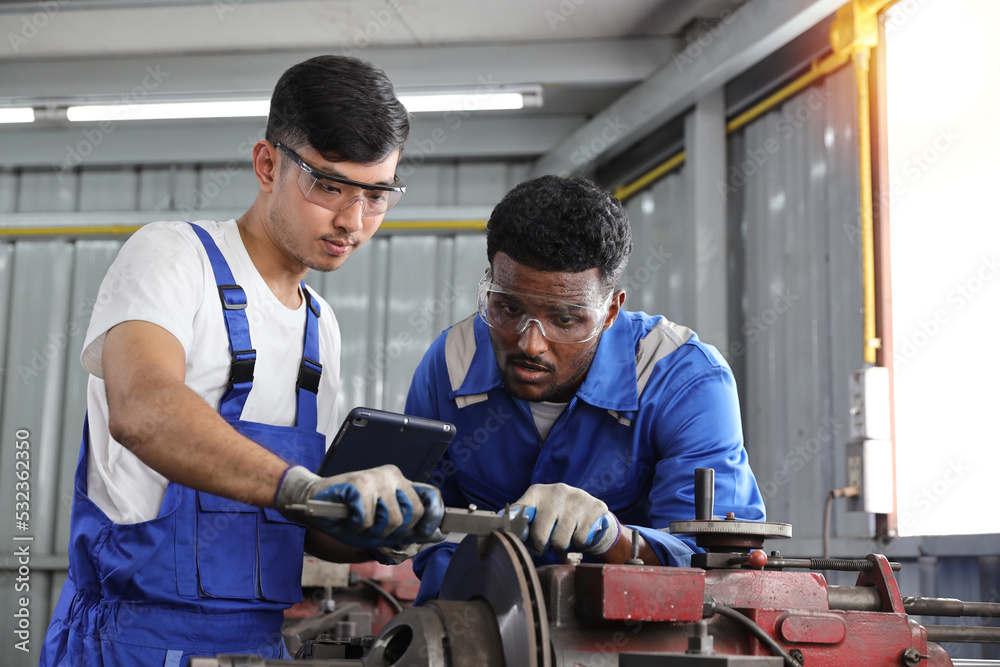 Multiethnic technicain mechanic or worker man in protective uniform using metal lathe machine operate polishing car disc brake at garage. Maintenance automotive and inspecting vehicle part concept